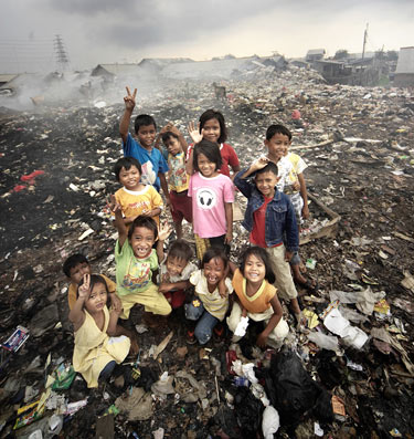 Several children stand happily on a large pile of trash at the city dump where they look for treasures.
