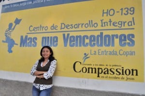 young woman in sweater vest leaning against Compassion sign
