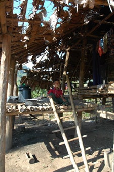young boy sitting inside a thatched bamboo home