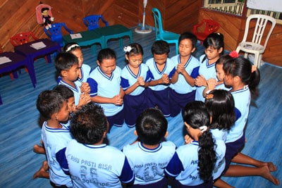 group of children in blue school uniforms in a circle praying