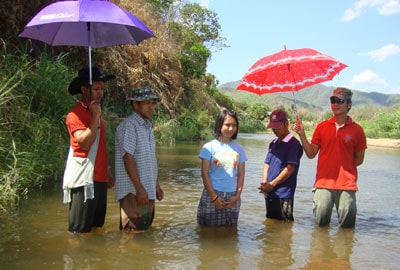 group of four men and one woman standing in water at river's edge