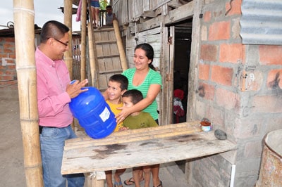 man handing a container of clean water to a woman and two boys