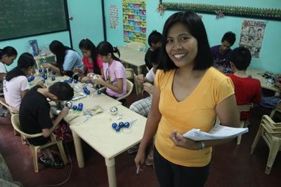 woman smiling in a classroom with children making crafts