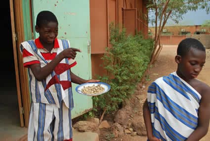 a boy in a red striped shirt carrying a plate of food pointing at another child