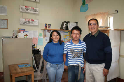 Jorge in a blue and white shirt standing in the Compassion office with two of the Compassion center staff