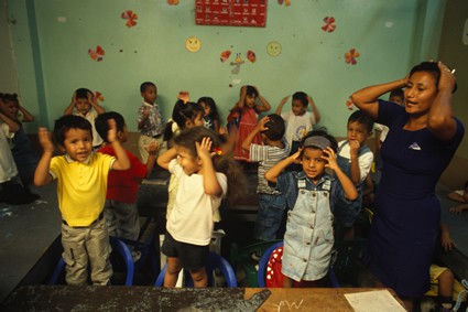 children inside a classroom each with hands on their heads