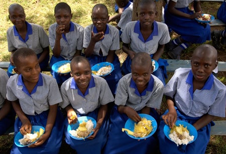 group of children in school uniforms sitting down to eat a meal