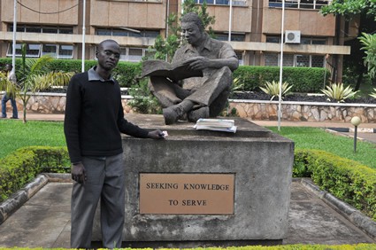 Lawrence standing by a statue seeking knowledge to serve by Makera University in Uganda