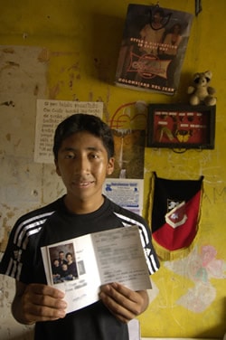 Young man in a black shirt standing in his home holding a letter and photo from his sponsor