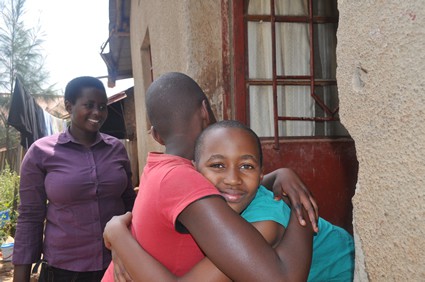 two children hugging as a smiling woman looks on