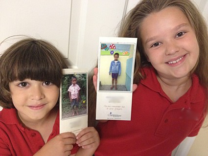 Two young girls in red shirts smiling holding photos of their sponsored children