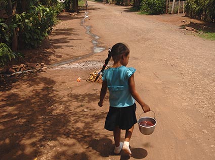 girl walking on road carrying a pail