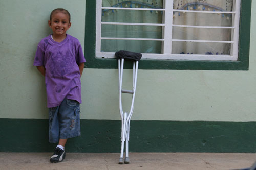 A girl stands against a wall with crutches next to her