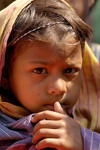 Young girl with a head covering, holding her thumb to her mouth