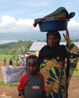 A child stands in front of a woman carrying a plastic tub on her head