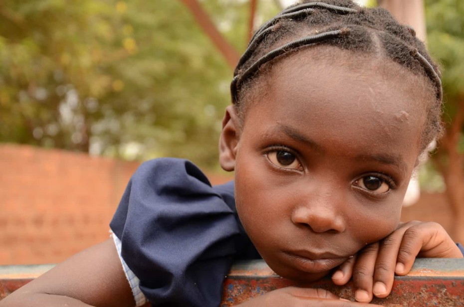 A tired girl leans on a fence in Burkina Faso