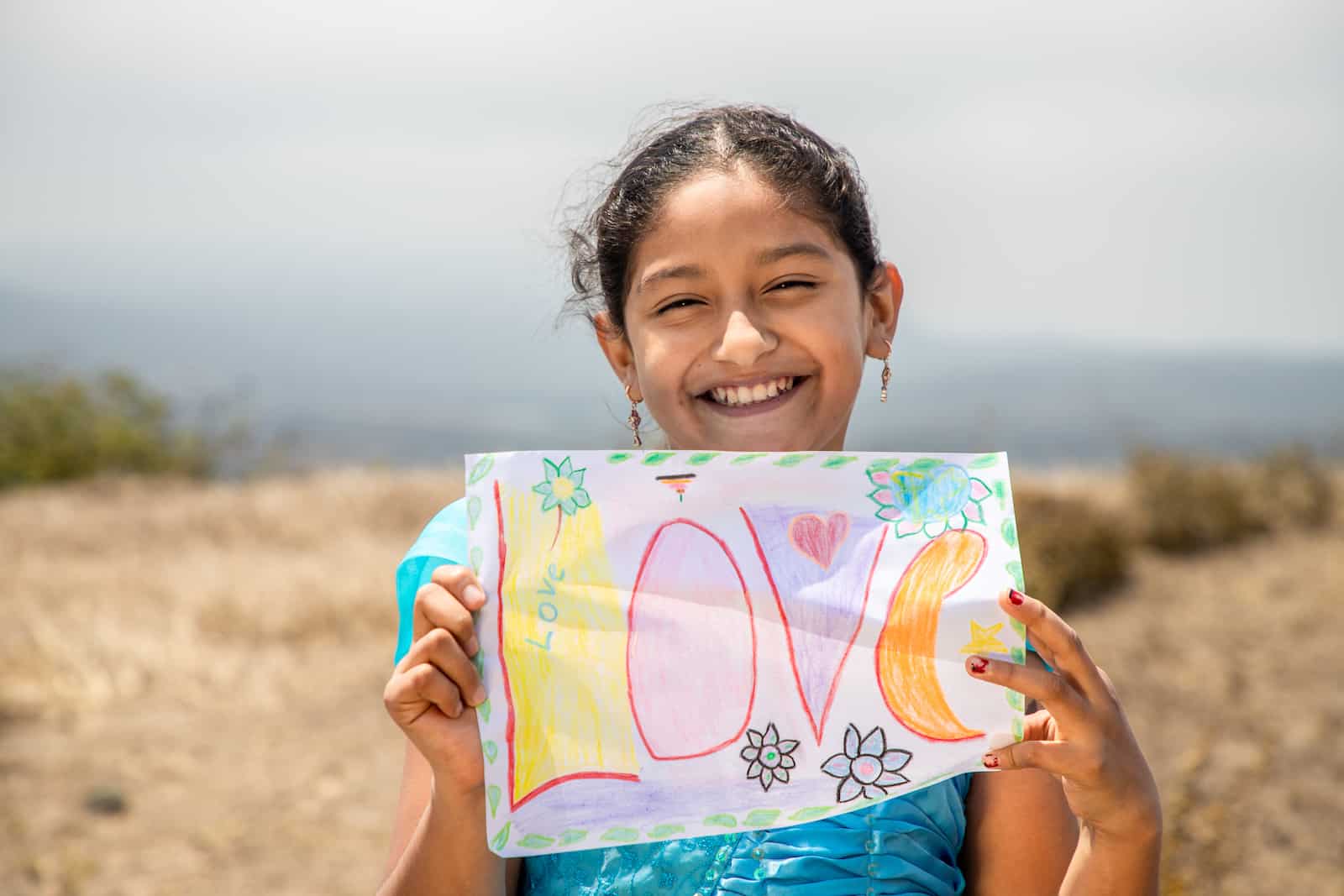 A girl stands outside holding a sign that says Love.