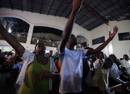 People in a crowded church singing and lifting their hands to praise God