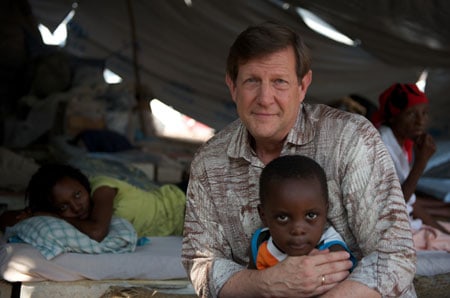 man hugging small child as two people look on in the background