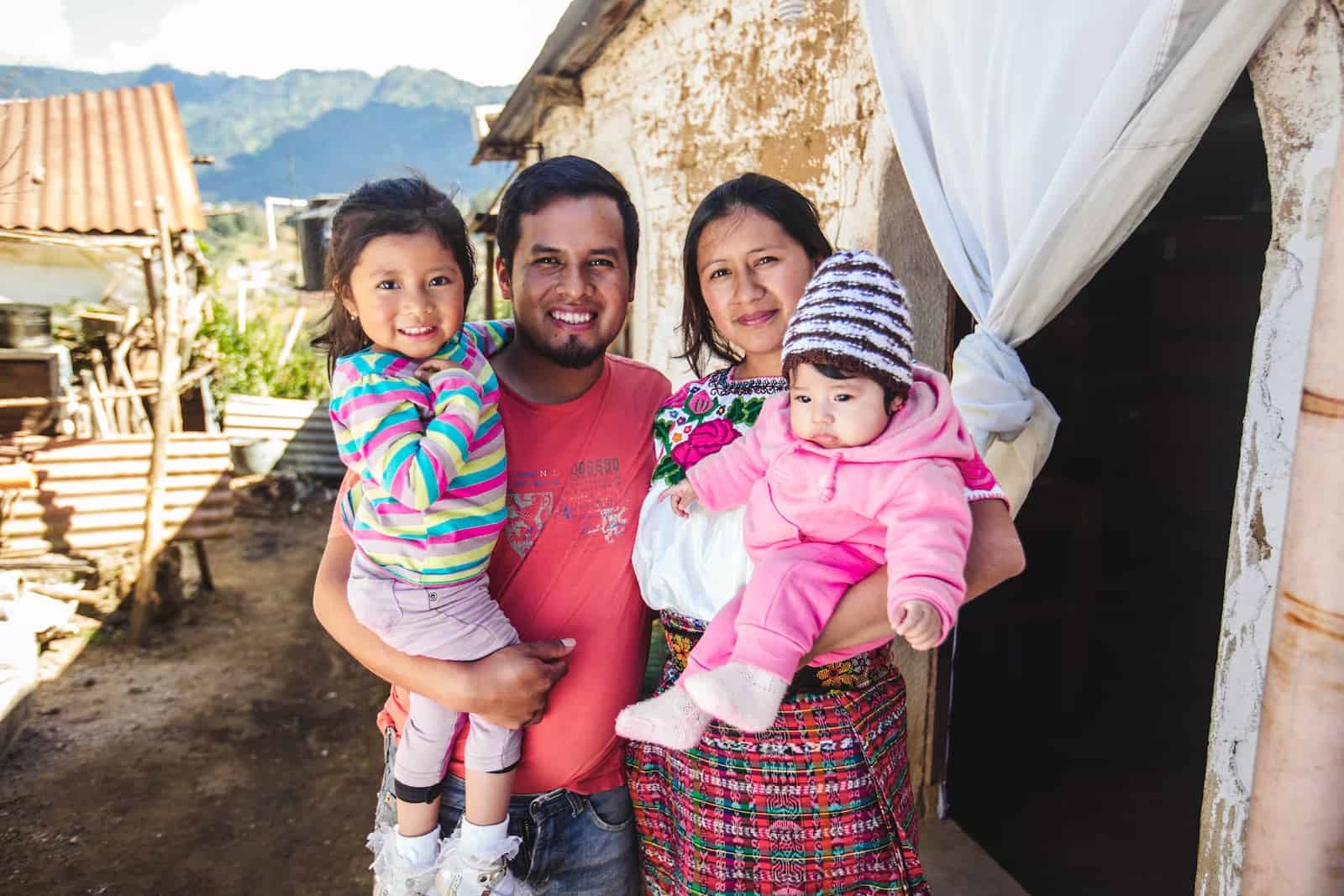 A family of four stands outside a brick home in Guatemala.