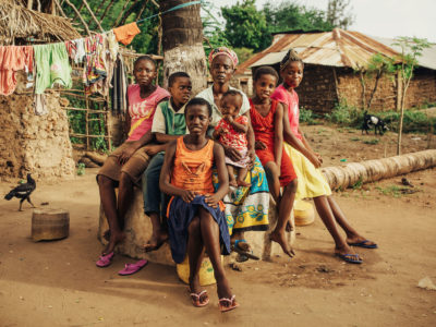 A large family sits outside of grass and mud homes in Kenya.