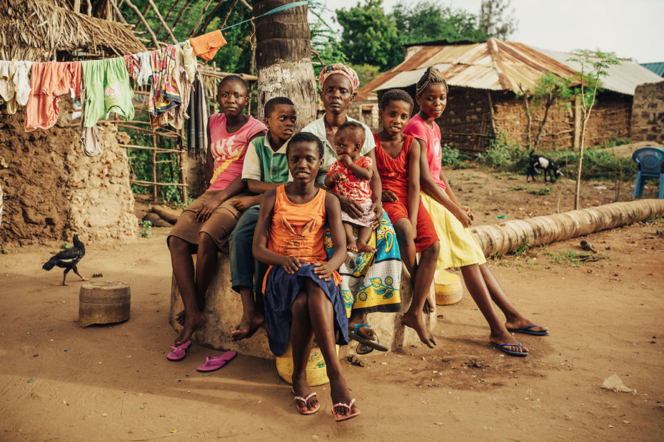 A large family sits outside of grass and mud homes in Kenya.