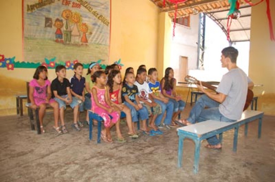 Man sitting on a bench playing guitar for a group of children in a classroom