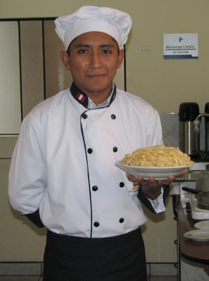 young man in chef's uniform holding a bowl of pasta