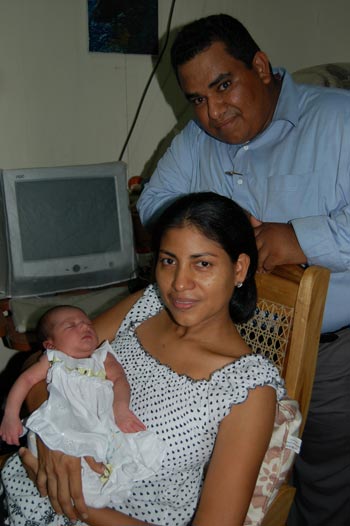 woman sitting in chair holding a newborn baby with man standing behind them