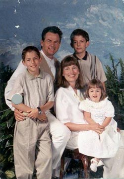 family photo of man and woman with girl on her lap and two boys standing