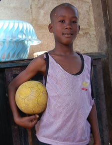 young boy wearing a tank top and holding a soccer ball
