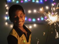 A boy holds a sparkler, surrounded by lights celebrating Christmas in El Salvador