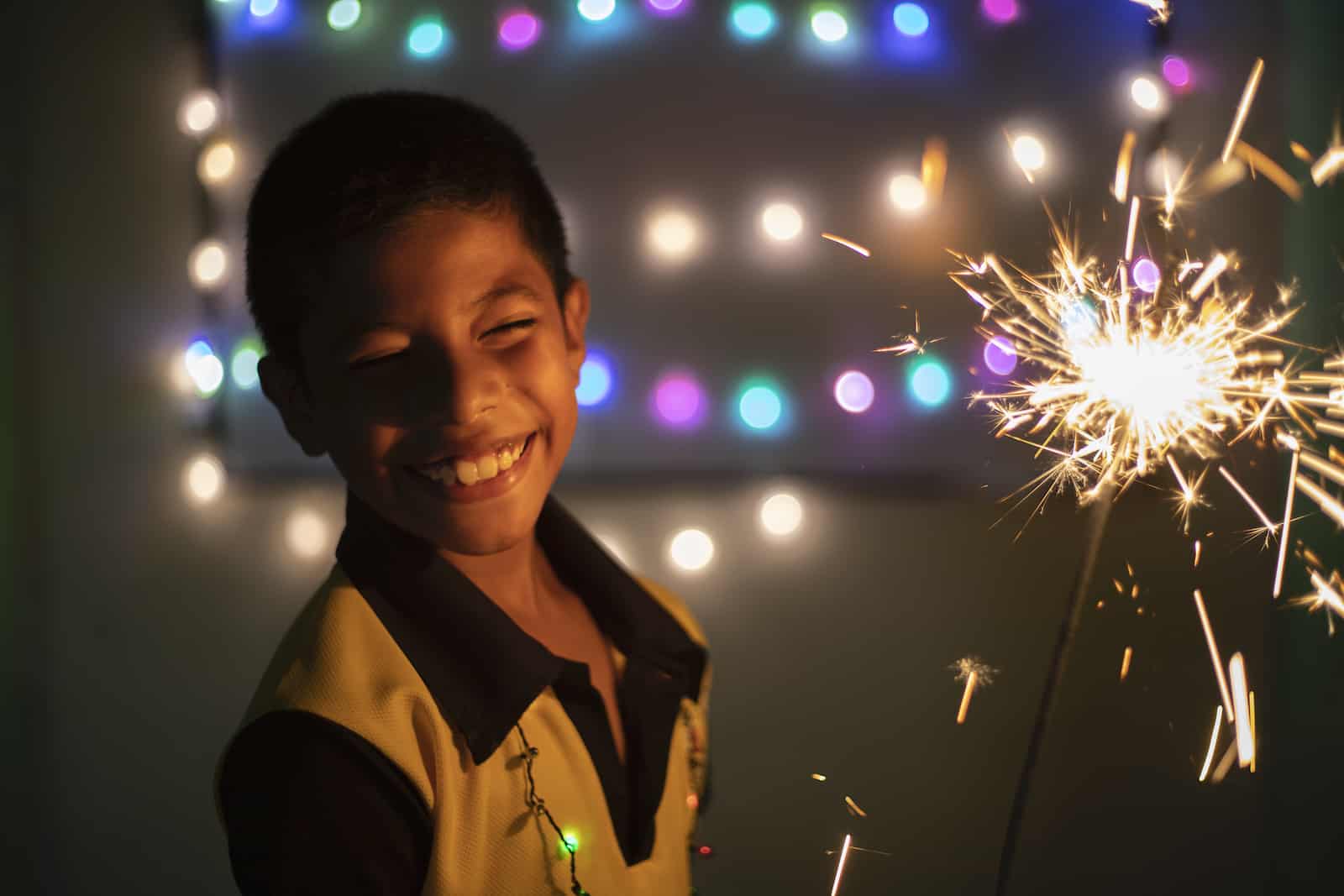 A boy holds a sparkler, surrounded by lights celebrating Christmas in El Salvador