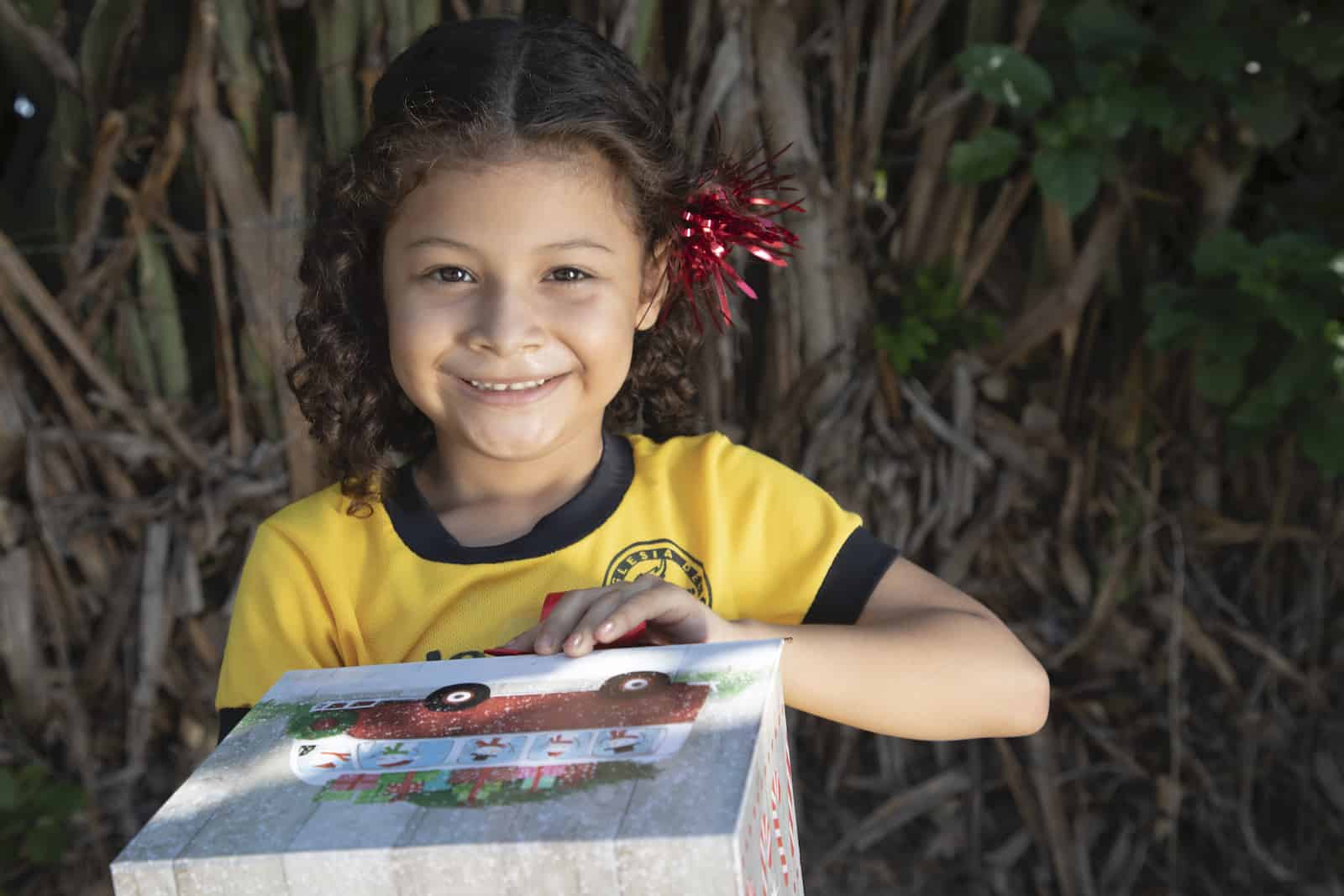 A girl in a yellow shirt holds a Christmas gift.