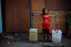 small girl carrying two containers of water on shoulders