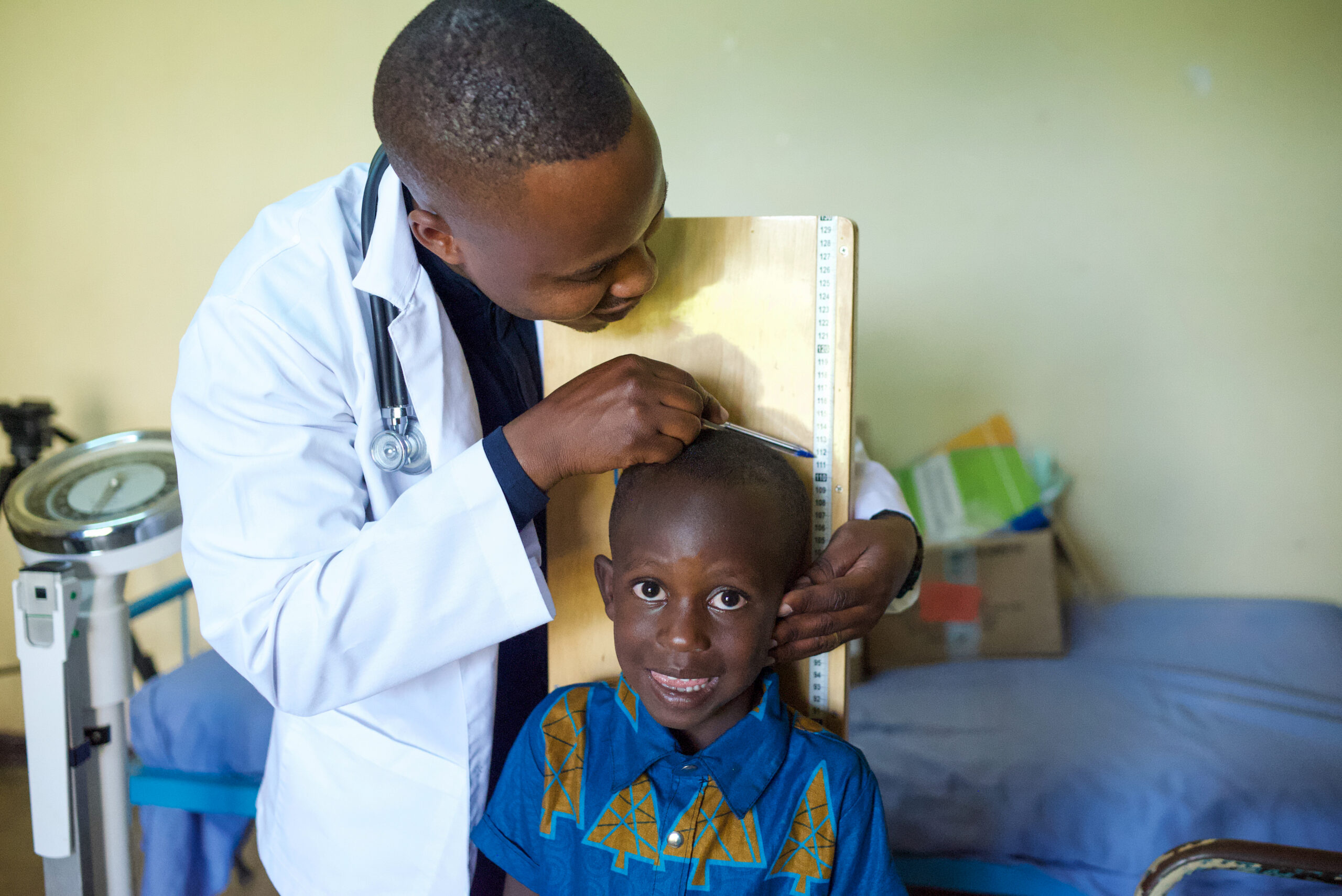 A young boy stands against a board while he’s measured by a doctor.