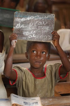 A boy holding up a slate with chalk writing on it