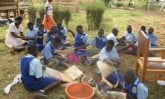Many children sitting outside making baskets.