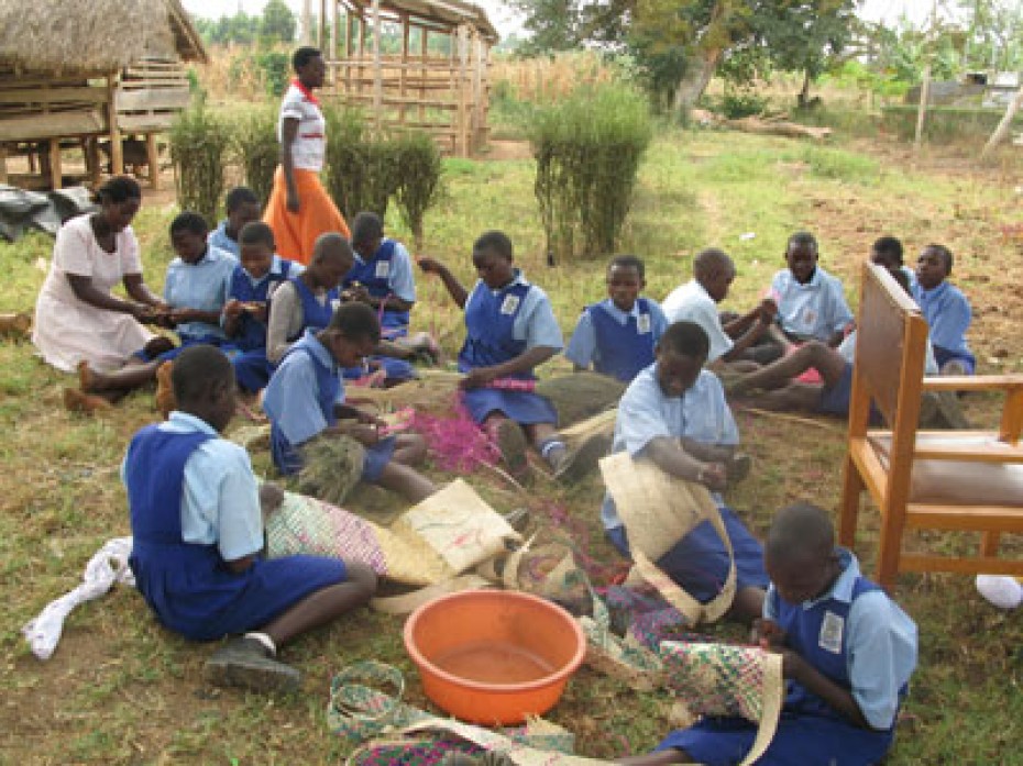 Many children sitting outside making baskets.
