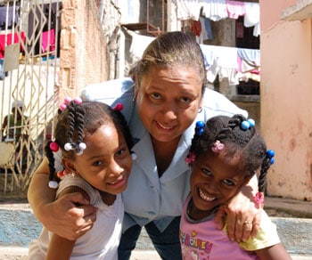 woman stooping over to hug two children