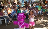 young girl hitting piñata in front of crowd of children