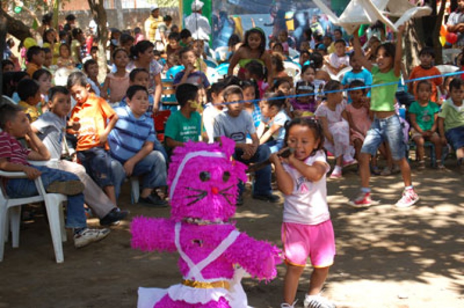 young girl hitting piñata in front of crowd of children