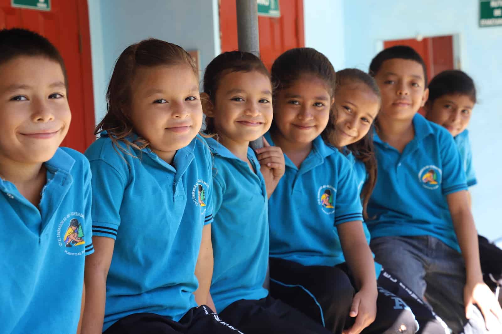 Children in blue shirts sit on a porch together.