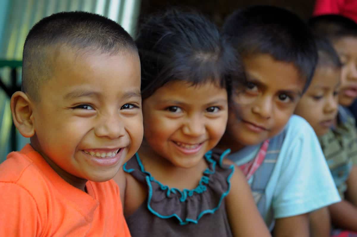 Three Salvadoran children smile at the camera.