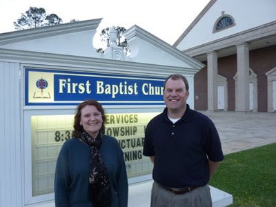 man and woman standing in front of church sign