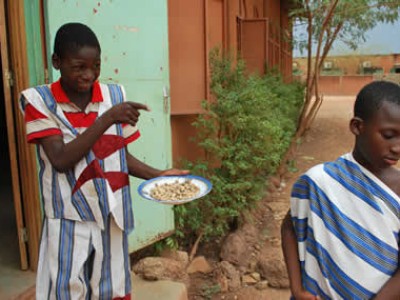 a boy in a red striped shirt carrying a plate of food pointing at another child