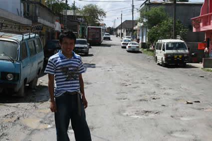 Young man standing in a neighborhood street in Guatemala filled with potholes