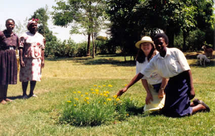 woman and young girl kneeling by flowers with two older women in background