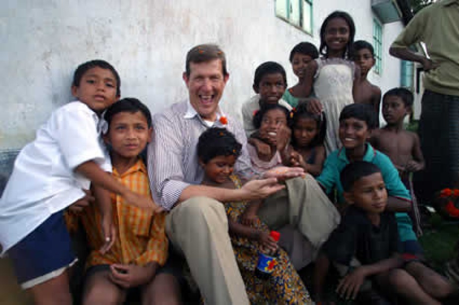 a man sitting up against a wall surrounded by happy children
