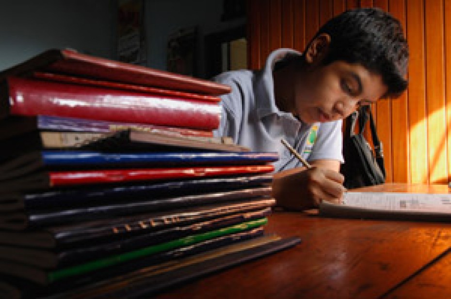 boy sitting and writing beside a stack of books